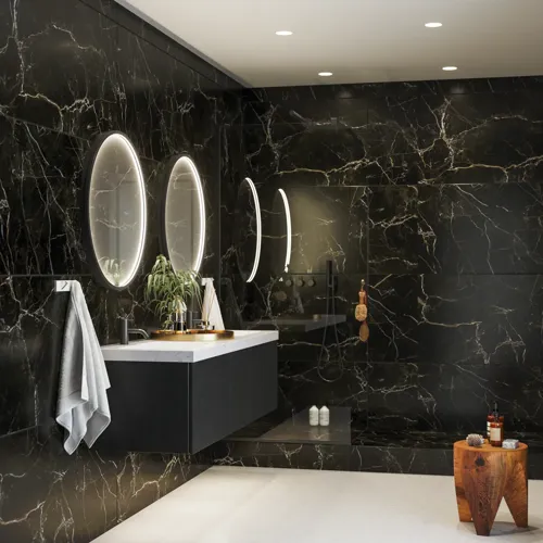 Elegante en moderne badkamer inspiratie met donkere marmeren muren, ronde verlichte spiegels met zwarte rand, wandgemonteerde wastafelkast met dubbele wastafel en een ruime douchehoek