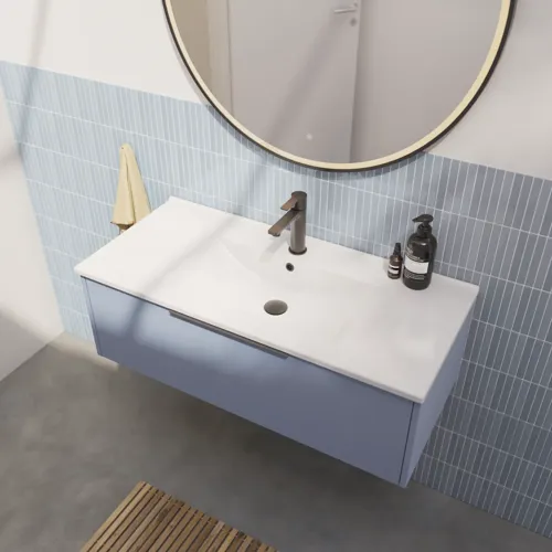 Badkamerinspiratie met langwerpige lichtblauwe tegels en betonnen vloer, elegant lichtblauw wastafelmeubel met mooie smalle strepen, strakke en dunne wastafel en een minimalistische ronde spiegel met zwarte rand en verlichting.