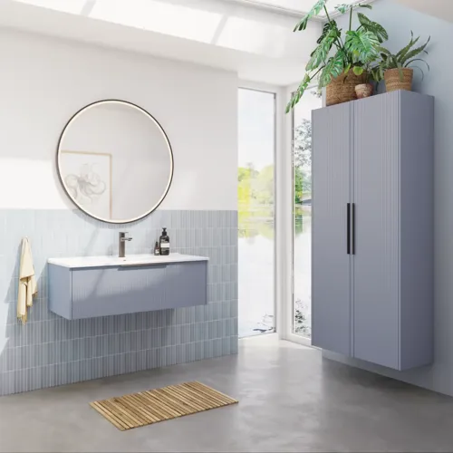 Badkamerinspiratie met lichtblauwe tegels en betonnen vloer, lichtblauw wastafelmeubel met smalle strepen, dunne wastafel, dubbele hoge kast en een ronde spiegel met zwarte rand en verlichting.