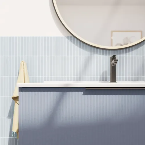 Badkamerinspiratie met langwerpige lichtblauwe tegels en betonnen vloer, elegant lichtblauw wastafelmeubel met mooie smalle strepen, strakke en dunne wastafel en een minimalistische ronde spiegel met zwarte rand en verlichting.